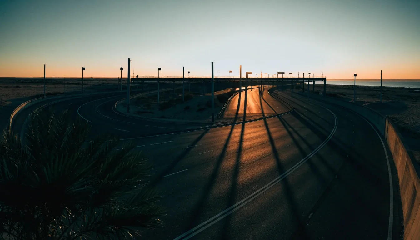 Gulf coastal highway interchange at dusk seen from an overpass, long shadows across the carriageway