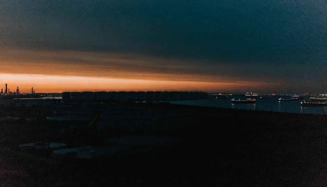 Refinery and storage silhouettes on the Gulf horizon at dusk with deep shadow in the foreground
